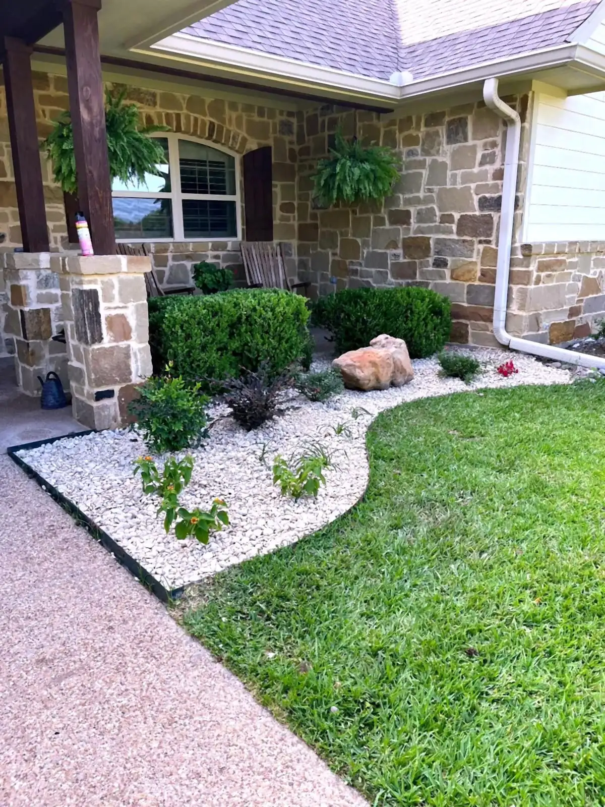A stone home in Central Texas with layered beds, river rock, and trimmed shrubs installed by H&M.