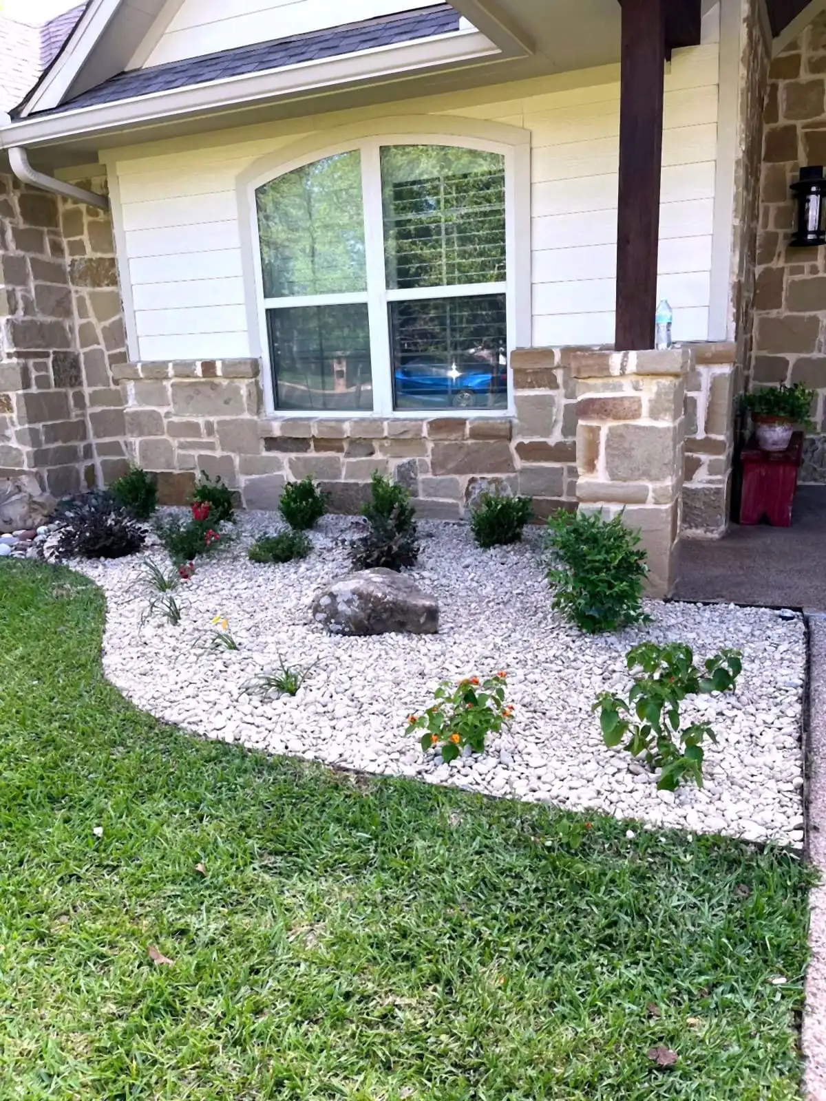 A residential foundation bed by H&M with white river rock, boulders, and flowering plants.